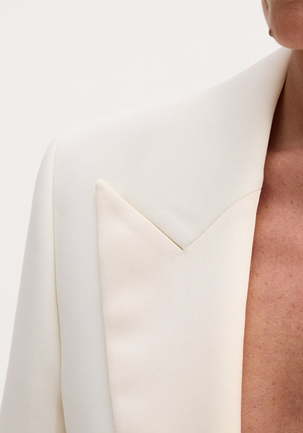 Cropped blazer | off white: Close-up of a tailored off-white wool blazer with contrasting satin peak lapels, hinting a concealed hook-and-eye closure.