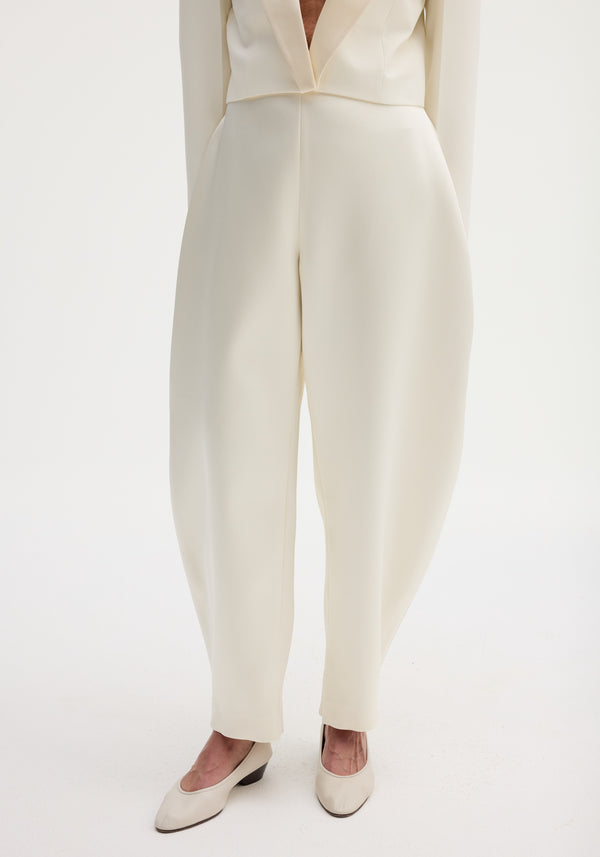 Lower half of a person in sculptural satin trousers with a high waist and balloon leg, paired with matching low-heeled pumps, showcasing a modern silhouette.