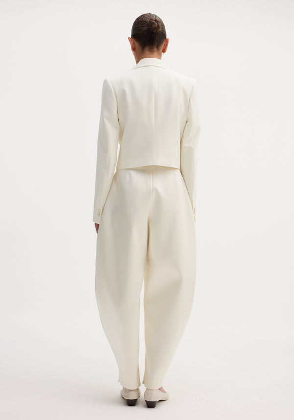 Sculptural satin trousers in ivory with a high waist and balloon leg, paired with a cropped blazer, creating a modern, minimal silhouette.
