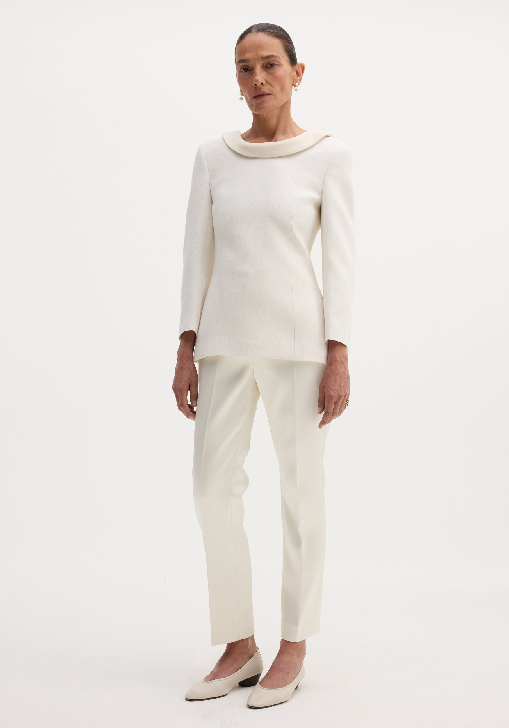 Woman wearing a Reversed blazer in winter white, featuring a satin neckline, welt pockets, button closures, and a strap across the open back.