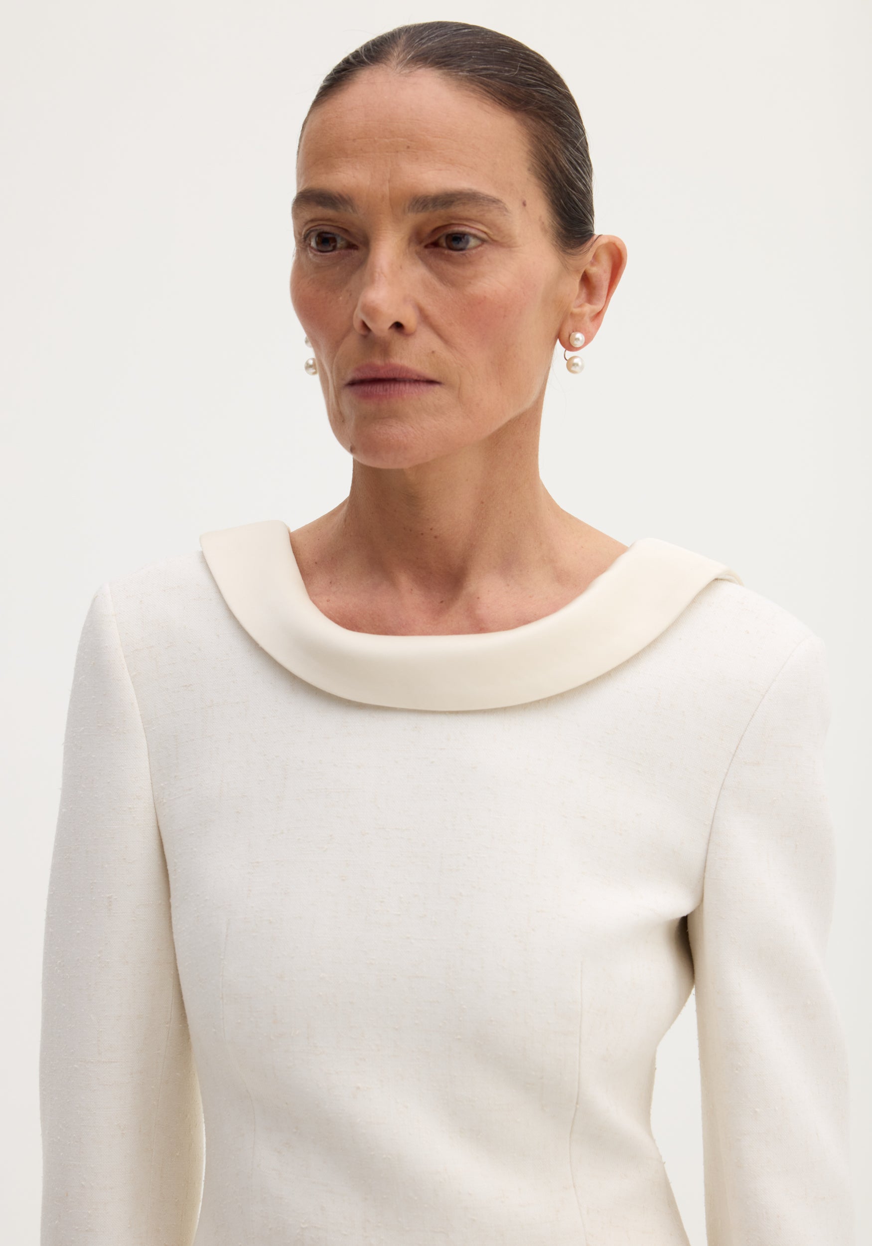Woman wearing a reversed blazer in winter white, featuring a softly draped neckline, drop pearl earrings, and structured fabric with button closures and welt pockets.