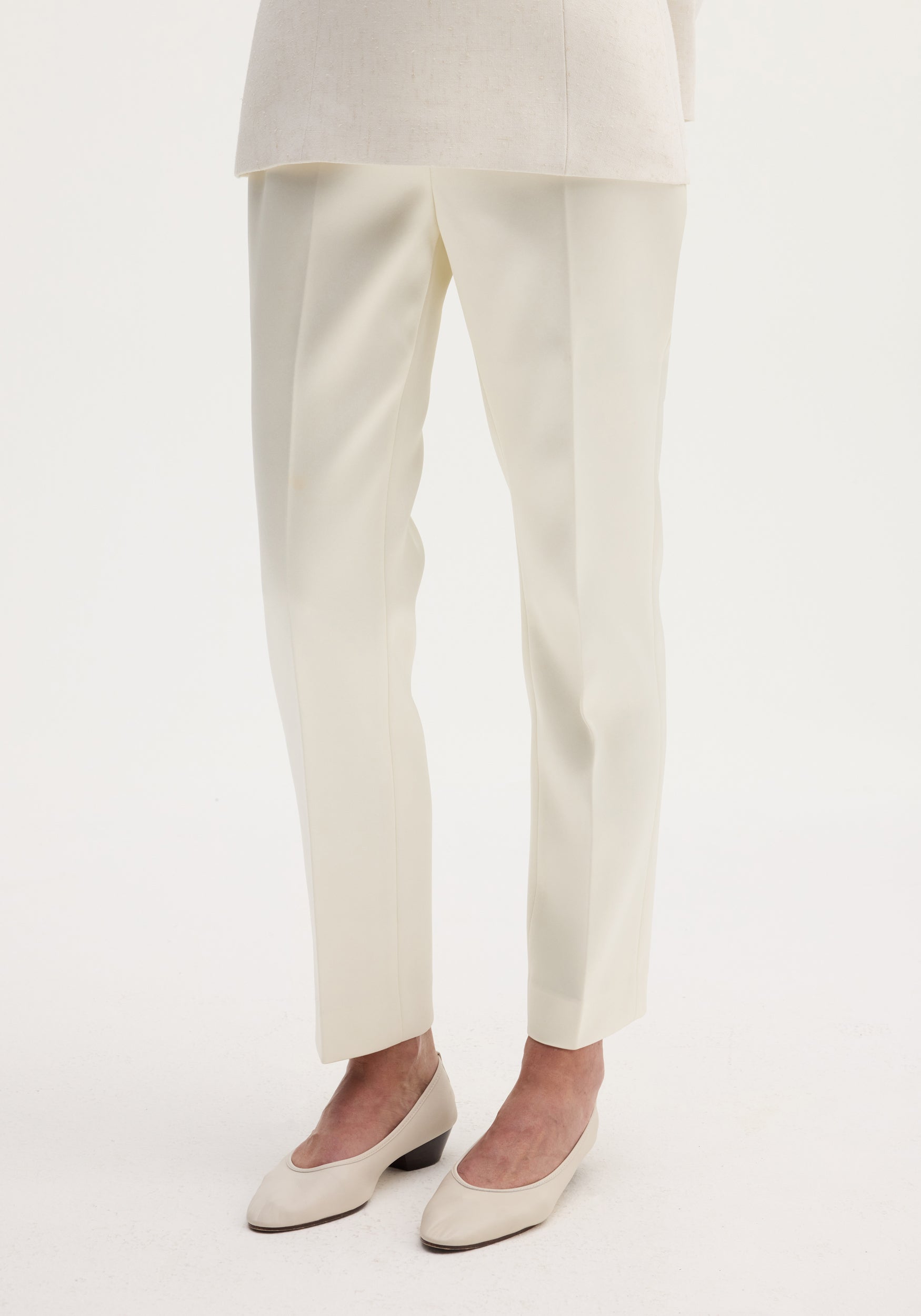 Cigarette leg satin trousers in ivory, featuring a high-rise fit and sharp center crease, paired with matching block-heeled pumps on a plain background.
