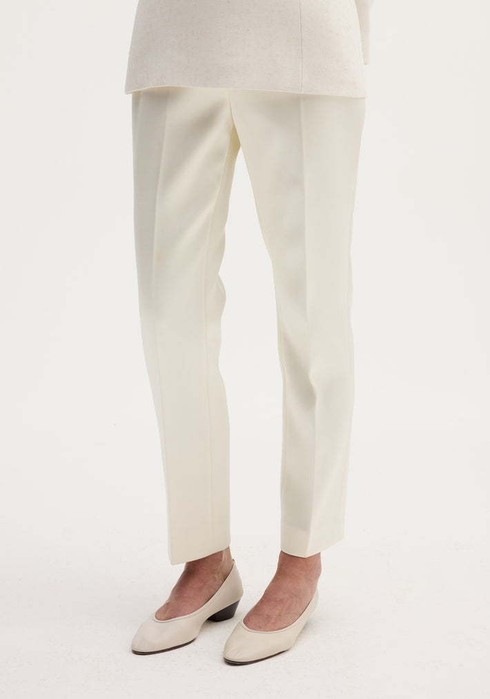 Cigarette leg satin trousers in ivory, featuring a high-rise fit and sharp center crease, paired with matching block-heeled pumps on a plain background.
