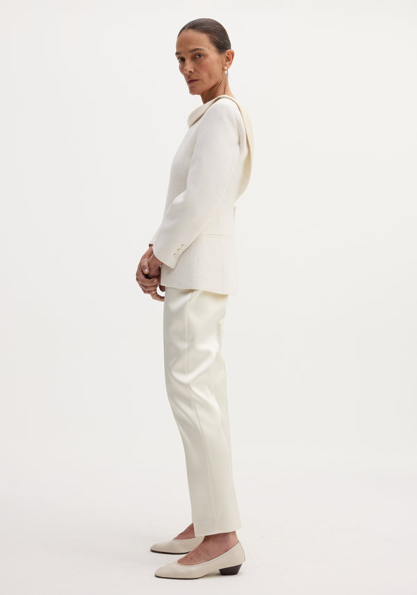 Woman in profile wearing a winter white reversed blazer with satin lapel, welt pockets, button closures; paired with slim-leg trousers and pearl earrings.
