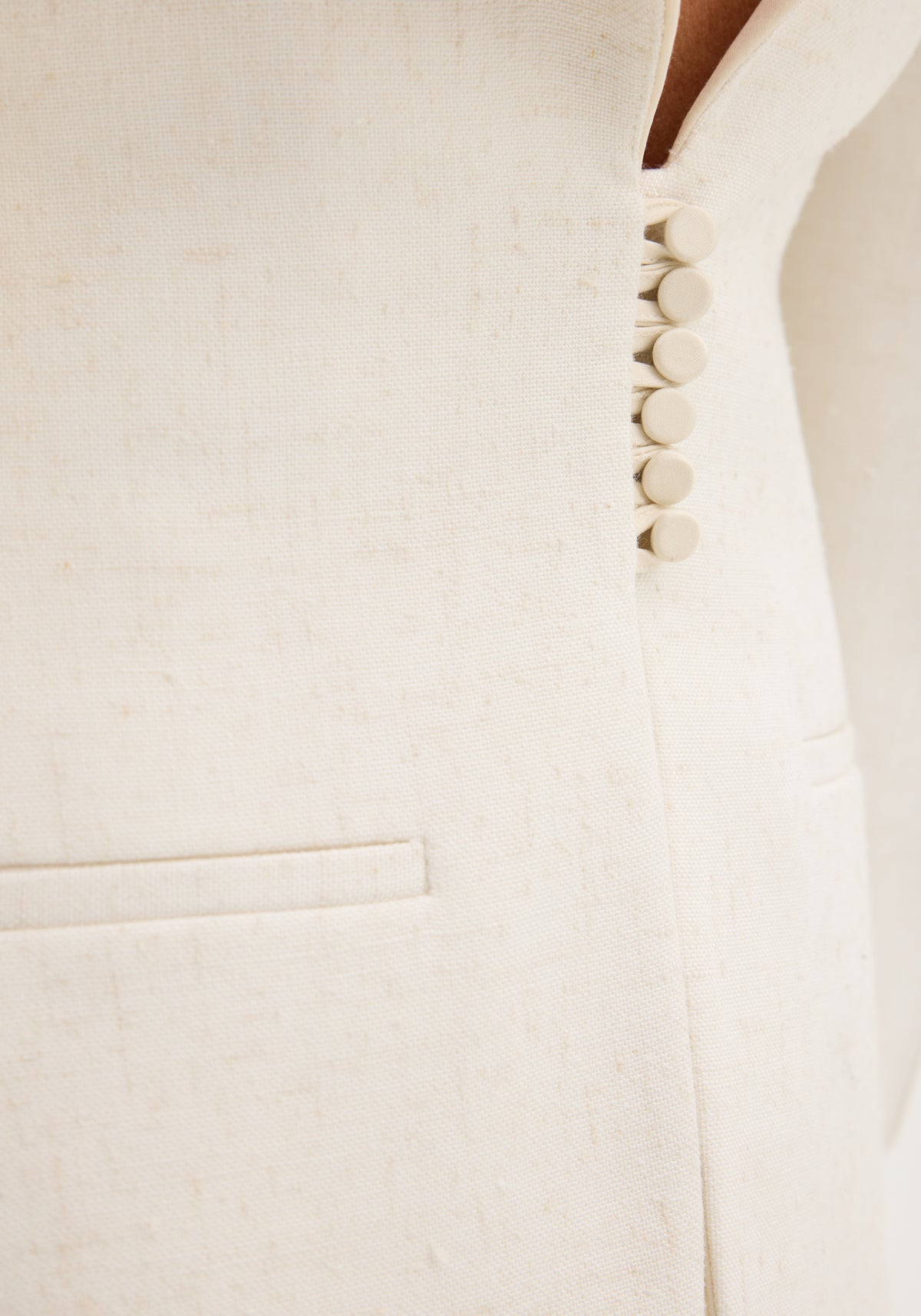Close-up of the Reversed blazer in winter white, showing the woven texture, fabric-covered buttons, and a welt pocket, highlighting its elegant, structured design.