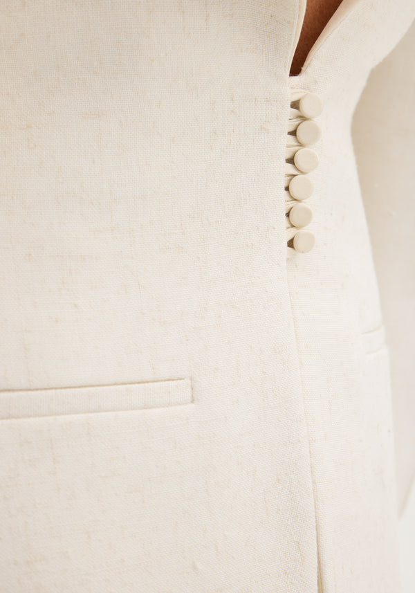 Close-up of the Reversed blazer in winter white, showing the woven texture, fabric-covered buttons, and a welt pocket, highlighting its elegant, structured design.