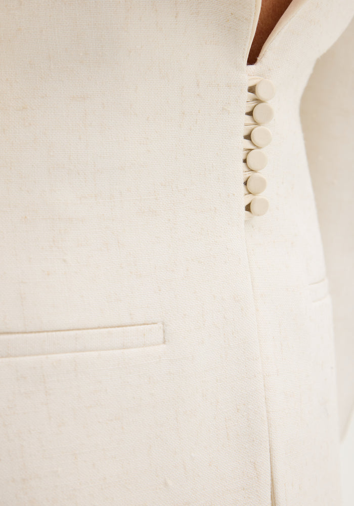 Close-up of the Reversed blazer in winter white, showing the woven texture, fabric-covered buttons, and a welt pocket, highlighting its elegant, structured design.