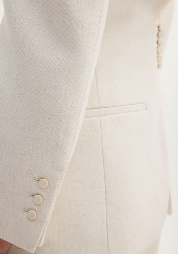 Reversed blazer in winter white, showcasing its textured slub fabric, sleeve’s covered buttons, and part of the welt pocket.