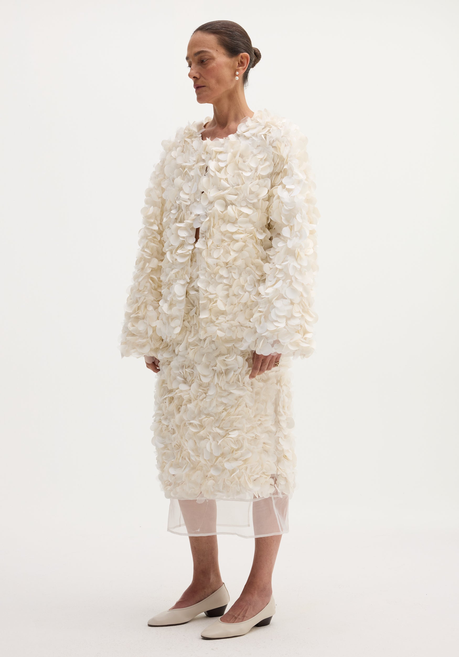 Woman modeling Handmade embellished skirt | ivory, with petal-like appliqués and silk organza hem, styled with matching pumps and pearl earring.