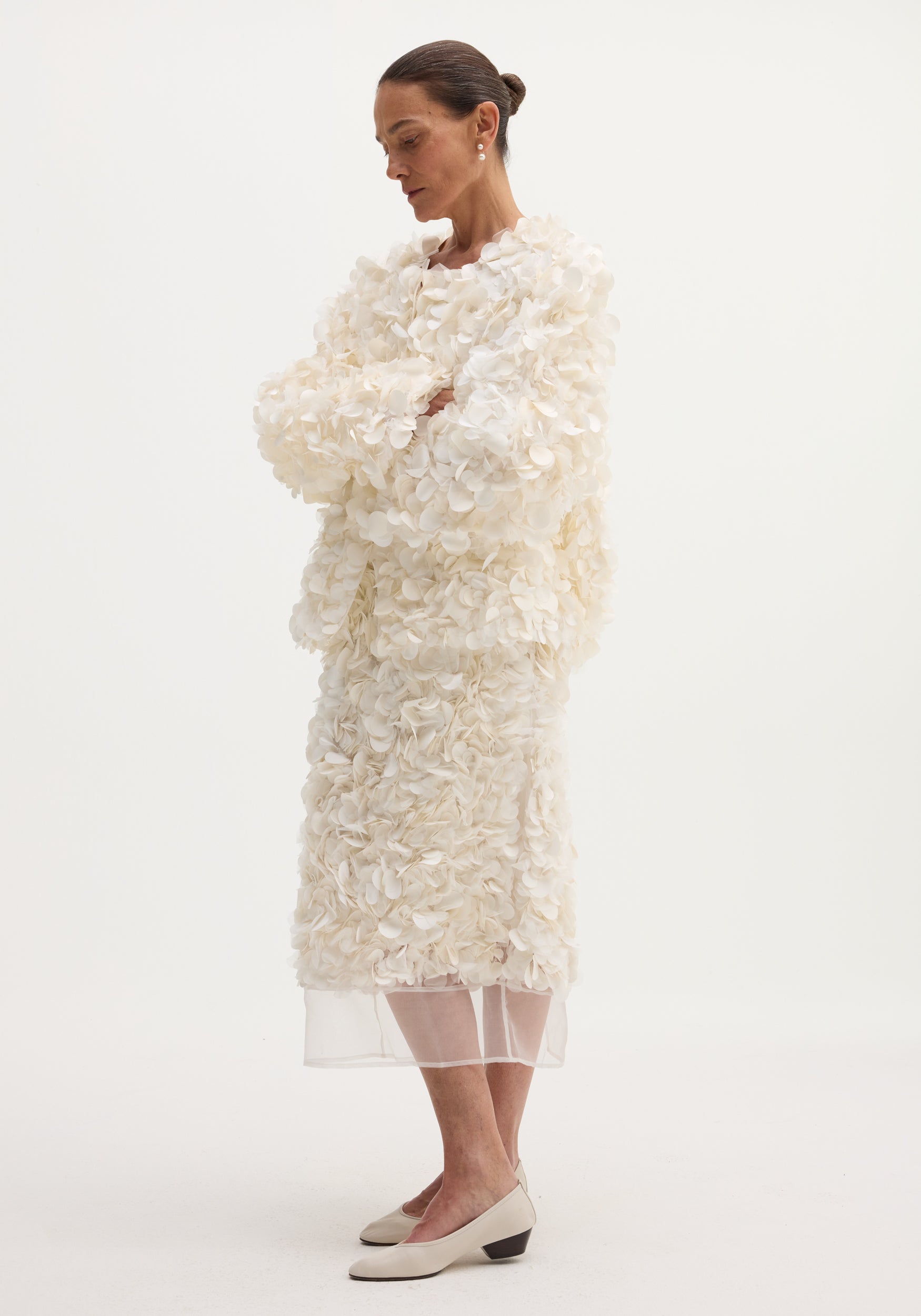 Handmade embellished skirt | ivory with textured petal-like appliqués and silk organza hem, worn with a matching coat, neat bun, and low-heeled shoes.