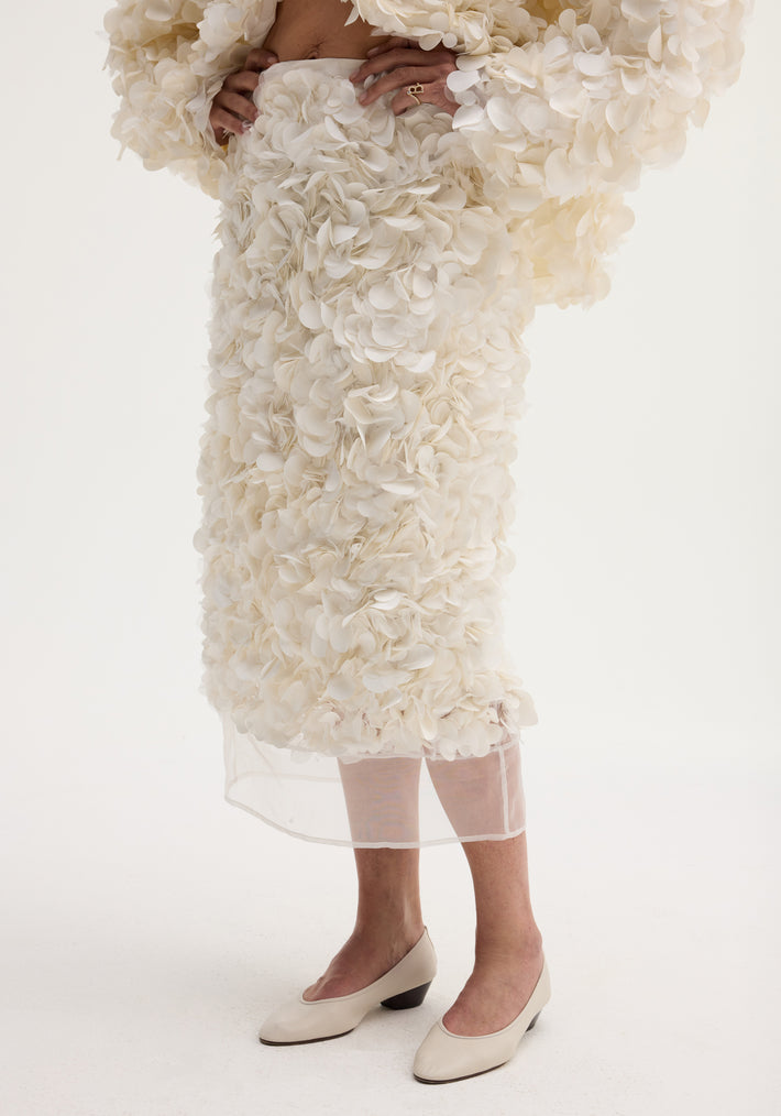 Handmade embellished skirt in ivory, featuring a voluminous knee-length design with delicate fabric appliqués and a refined silk organza hem, modeled with cream low-heeled pumps.