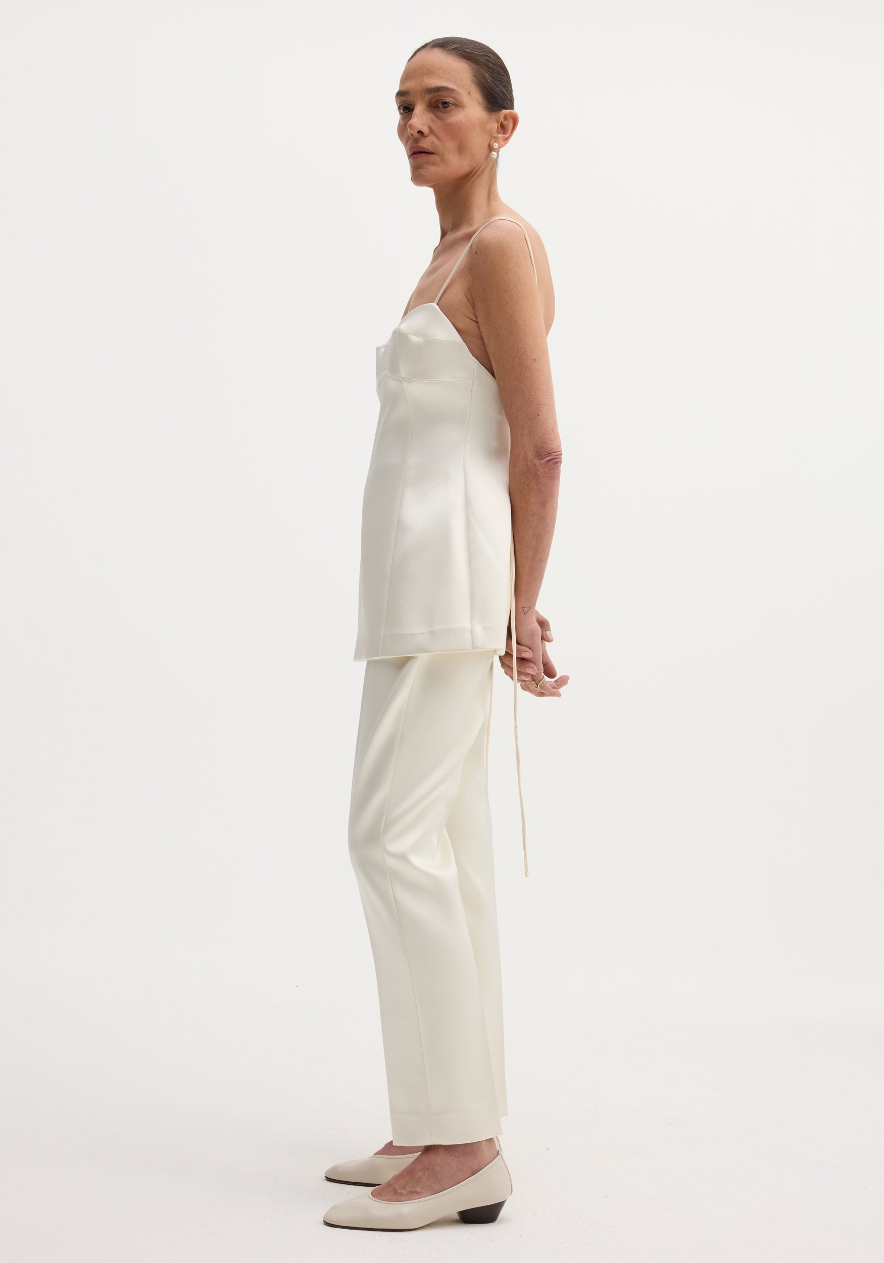 Satin bustier top in ivory showcased on a model with a fitted waist, bustier-style stitching, and adjustable straps, paired with matching straight-leg trousers.