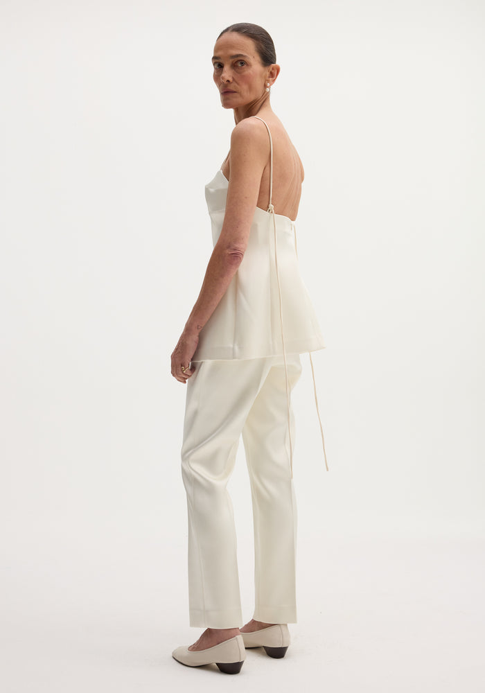 Model wearing Satin bustier top | ivory, showcasing its low-back design, bustier stitching, and long adjustable straps, paired with matching trousers and pointed-toe pumps.
