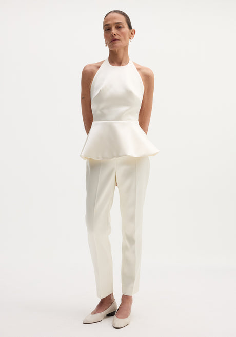 Model wearing Sculptural satin halter top with a fitted bodice and peplum, paired with matching tailored trousers and low-heeled pumps.