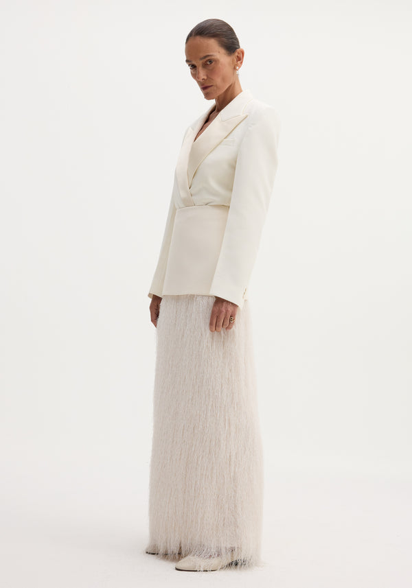 Model wearing Fringe skirt in ivory with floor-length fringe detail, tailored blazer, drop pearl earrings, and point-toed shoes, showcasing minimalist elegance.