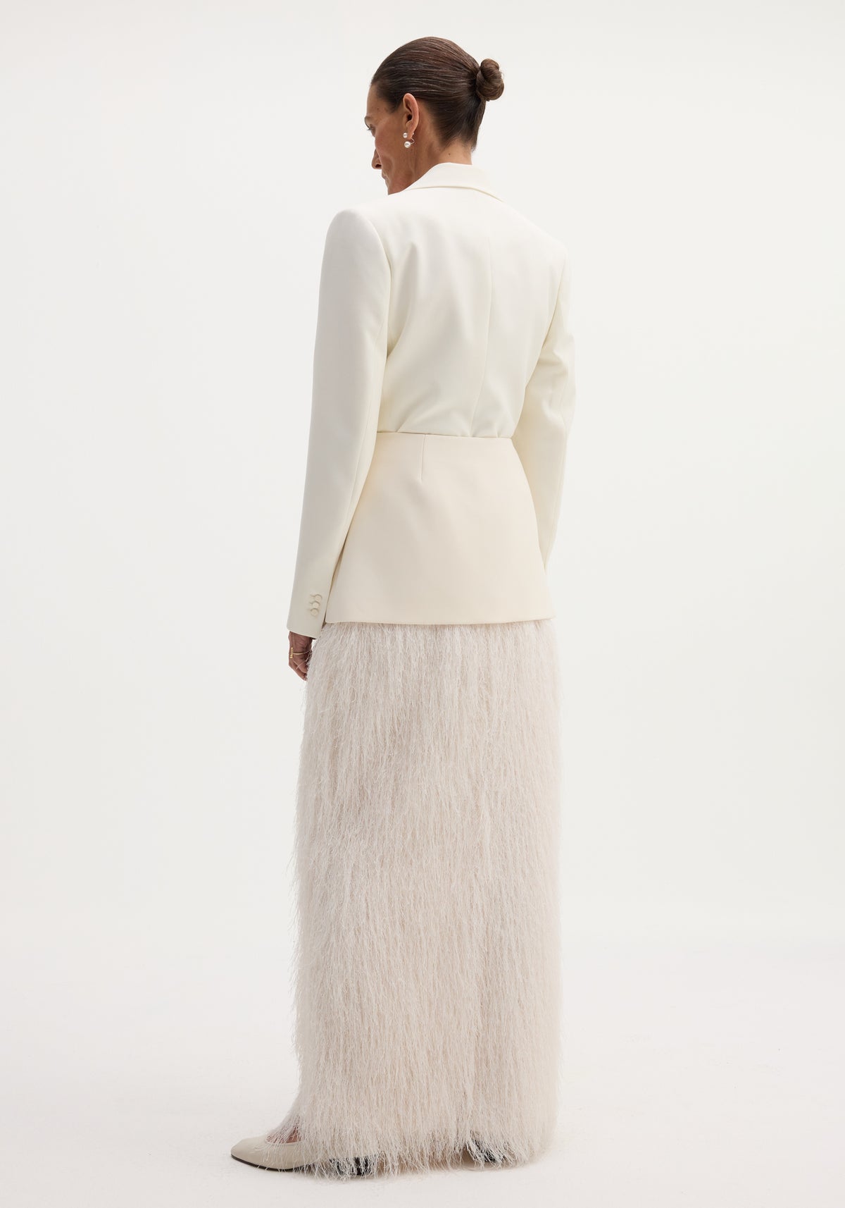 Model in off-white blazer showcasing the Fringe skirt | ivory, featuring a fitted wool upper and full-length fringe, with pointed-toe heels visible.