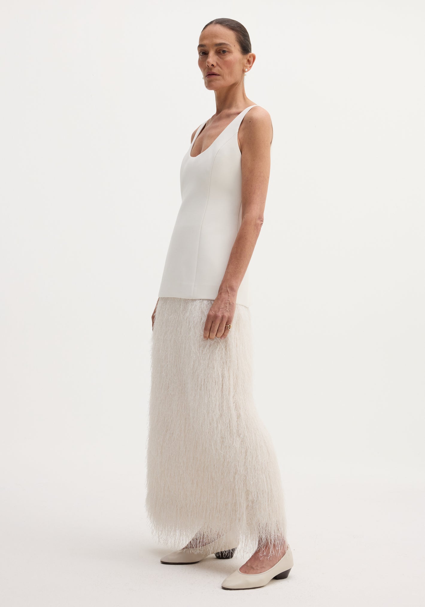 Tall woman in ivory Fringe dress, featuring a fused wool bodice and full-length fringe skirt, paired with cream pumps and minimal jewelry against a white background.