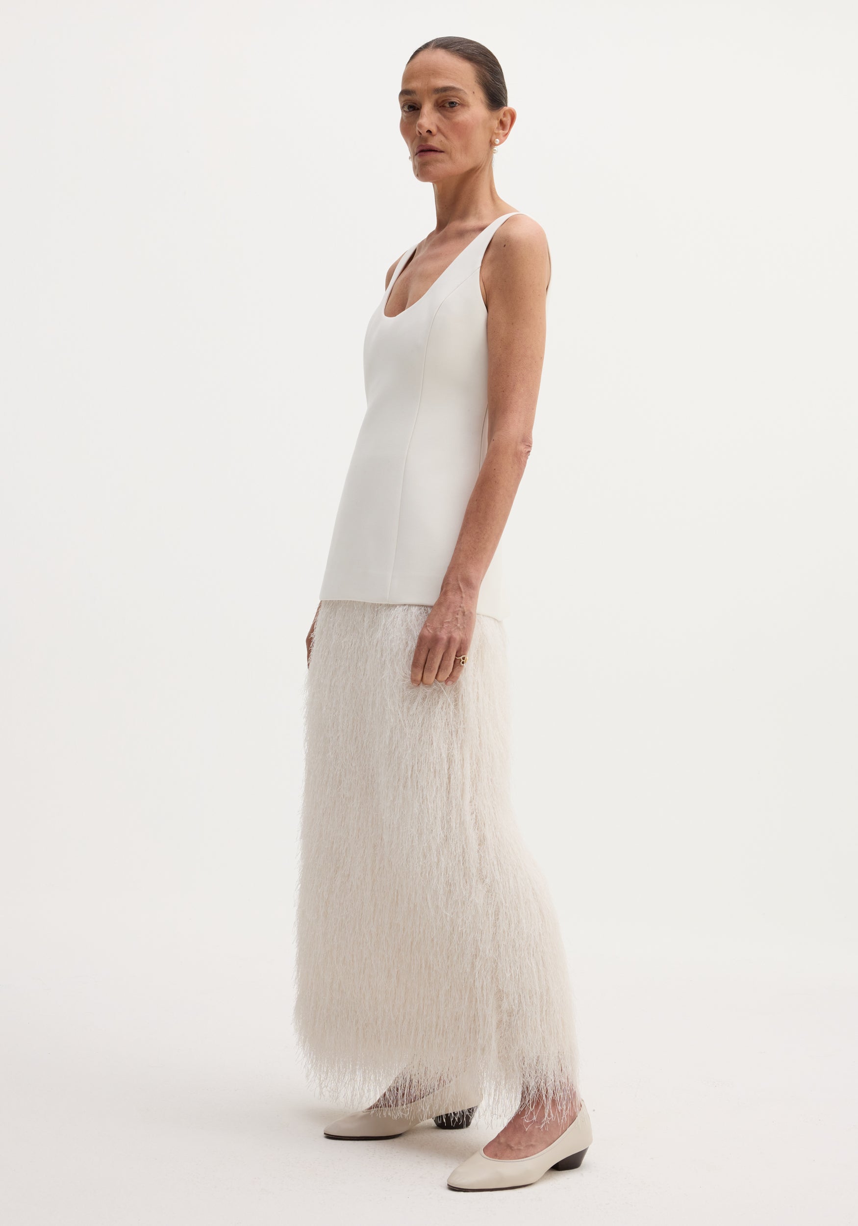 Tall woman in ivory Fringe dress, featuring a fused wool bodice and full-length fringe skirt, paired with cream pumps and minimal jewelry against a white background.