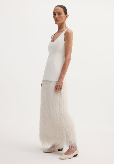 Woman models Fringe dress | ivory with a structured fused wool bodice and floor-length feathery fringe skirt, accessorized with pearl earrings and rings.