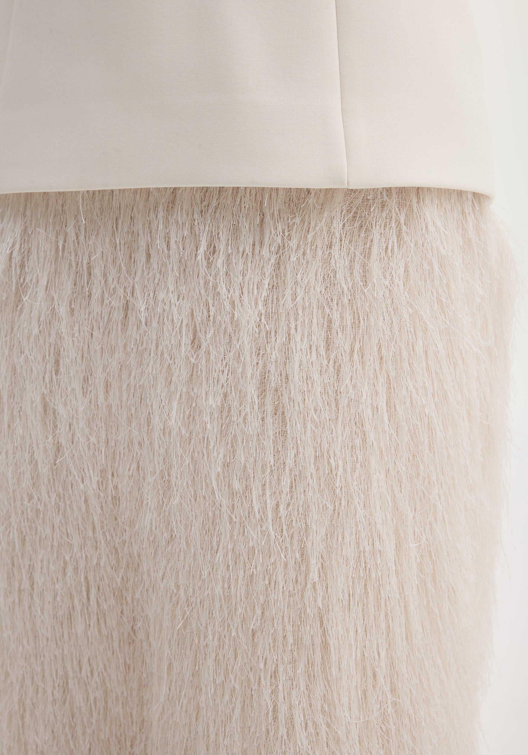 Close-up of the Fringe dress in ivory, featuring straw-like fibers forming a textured, full-length fringe skirt attached to a smooth fabric band.