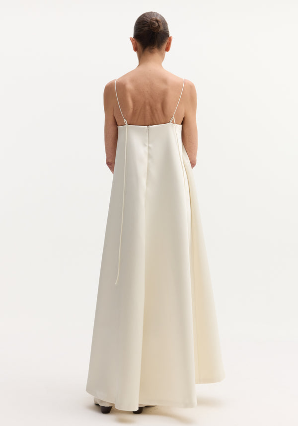 Woman in Voluminous satin dress | ivory, seen from behind, wearing a floor-length gown with adjustable spaghetti straps tying at the back, and button details.