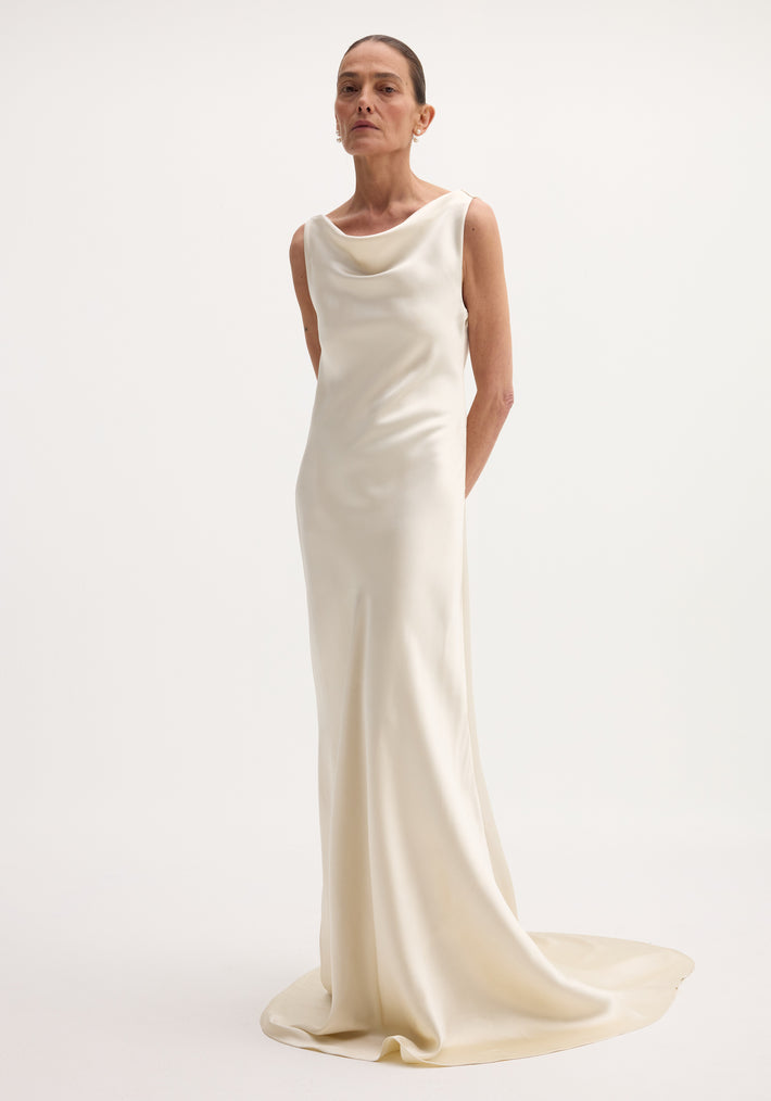 Tall model in an ivory Draped satin dress with train, featuring a cowl neckline, sleeveless design, and elegant drape, accessorized with pearl earrings.