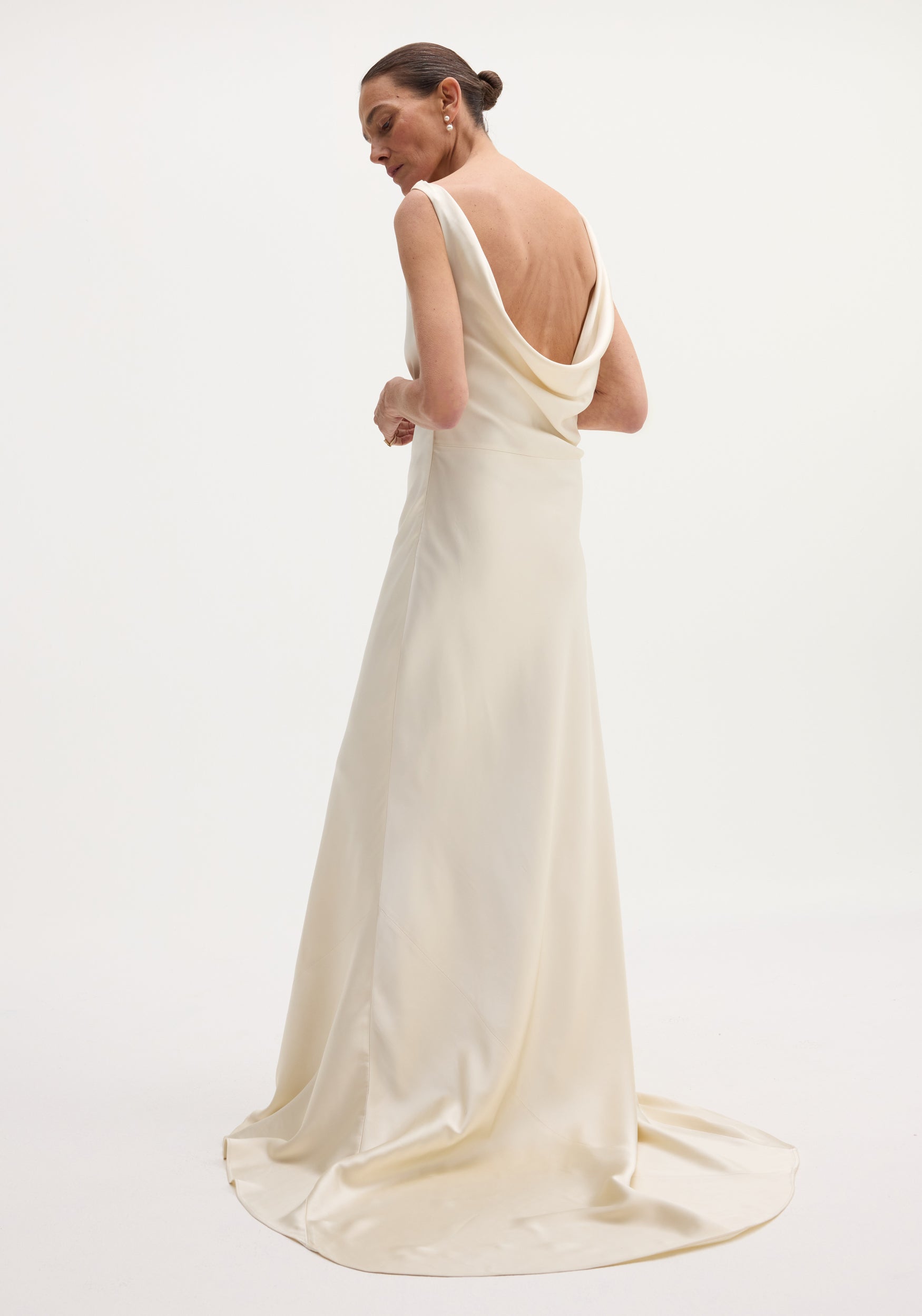 Woman in ivory Draped Satin Dress with Train, featuring a sleeveless design, cowl back, and a pooling train, accessorized with pearl earrings.