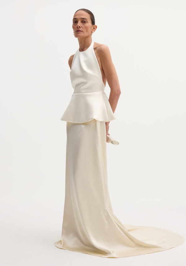 Model wears Sculptural satin halter top with separate silk skirt, featuring a peplum waist, open back, pooling skirt, and minimal pearl earrings.