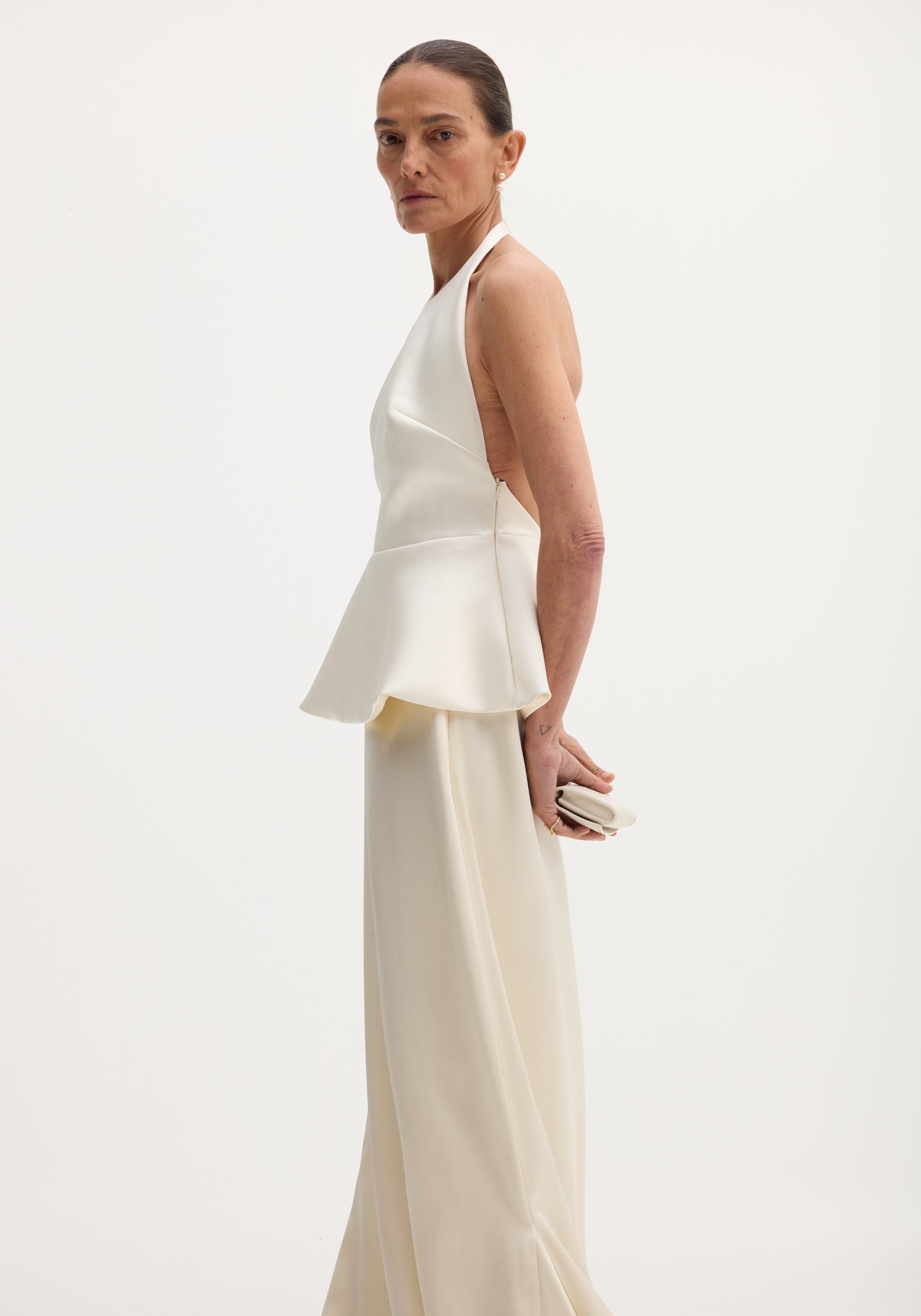 A model showcases the Sculptural satin halter top with separate silk skirt in ivory, featuring a fitted bodice, peplum waist, and elegant matching skirt.