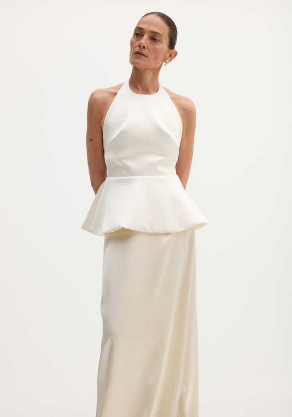 Person wears Sculptural satin halter top with separate silk skirt in ivory, showcasing a fitted bodice, peplum waist, and long, elegant draped skirt.
