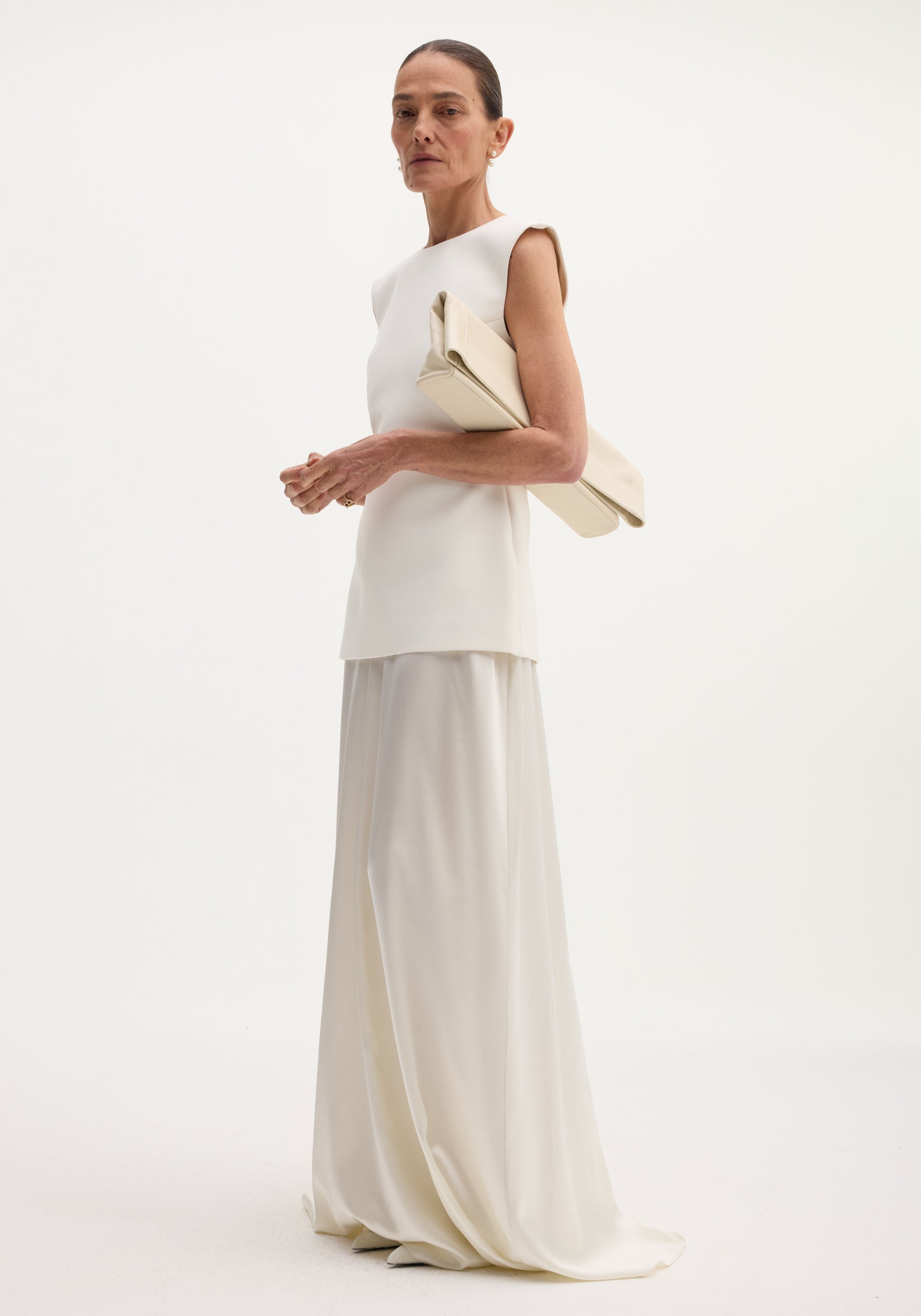 Model in Classic signature dress with satin silk skirt | ivory, featuring a structured bodice, open back, and flowing long skirt, accessorized with an oversized clutch.