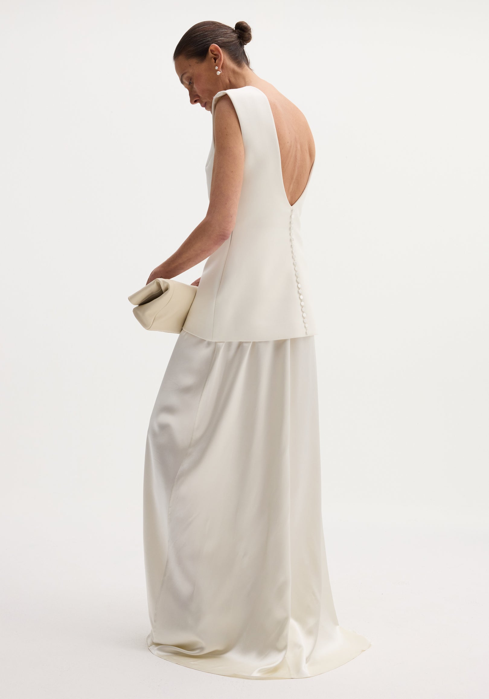 Profile view of a model in a Classic signature dress with satin silk skirt | ivory, featuring an open back, structured bodice, and long, flowing skirt.