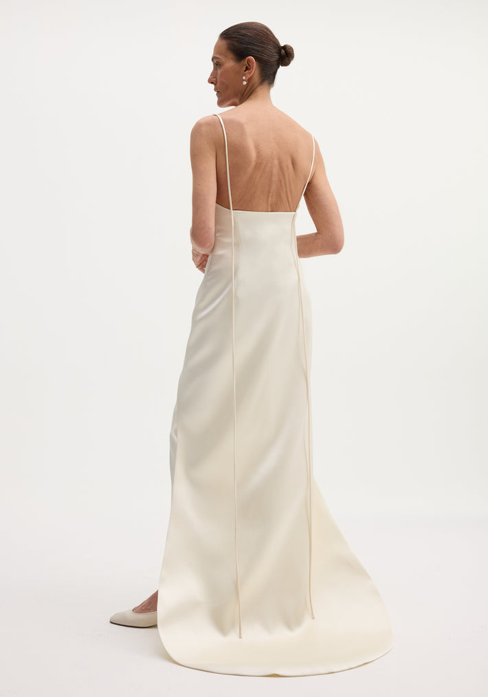Woman in an ivory satin bustier dress with a train, spaghetti straps, open back, and drop earrings, standing against a white background.