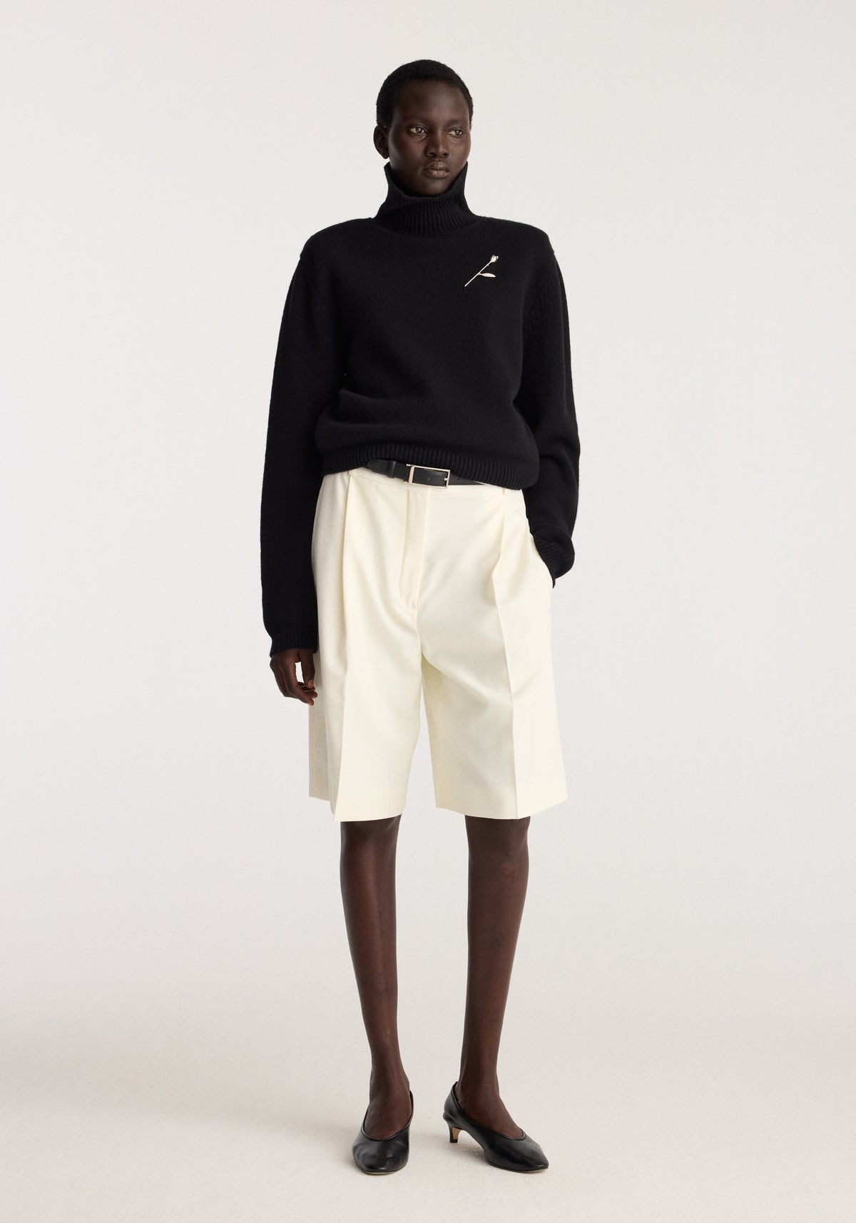 Tulip silver brooch | silver pinned to a black turtleneck sweater, modeled with cream shorts and black shoes in a studio setting