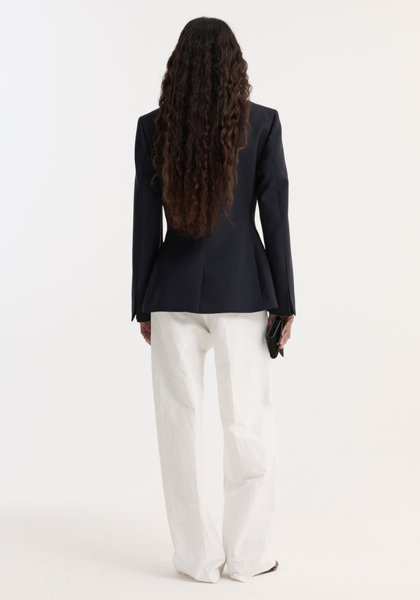 Back view of a person wearing the Hourglass shaped blazer, showcasing its sharp notch lapel, peplum waist flare, and high-waisted white trousers.
