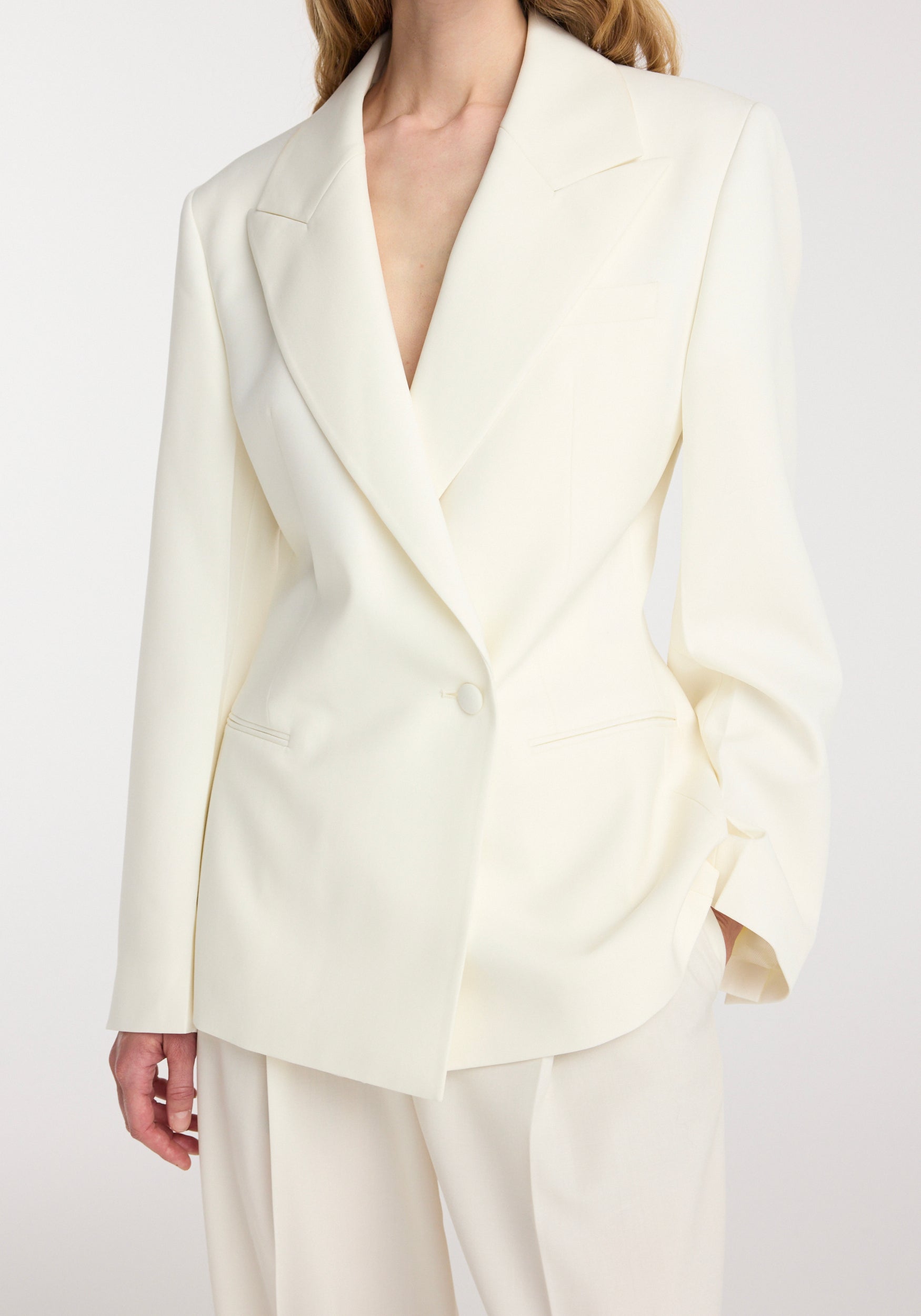 Model wearing an off white hourglass shaped blazer | off white with a tailored fit, single-button closure, wide lapels, and long sleeves paired with matching trousers.