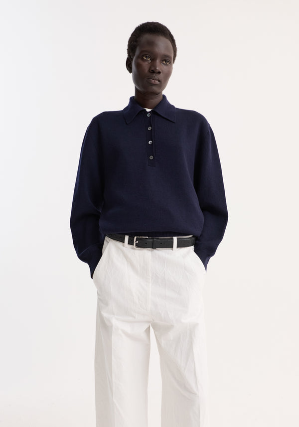 Merino wool polo in navy, featuring a structured collar and three-button closure, paired with high-waisted white trousers and a black belt.