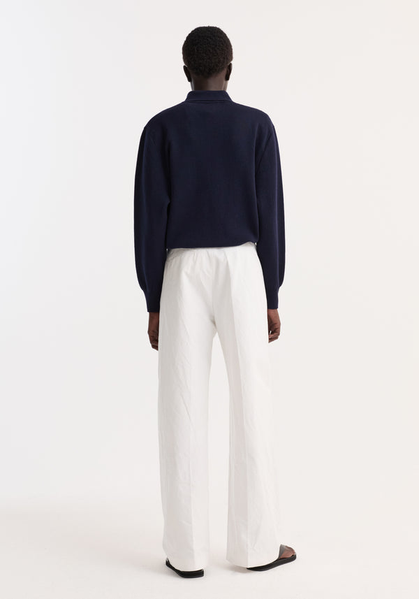 Rear view of a person wearing a Merino wool polo in navy, featuring a structured collar and three-button closure, paired with high-waisted wide-leg trousers.