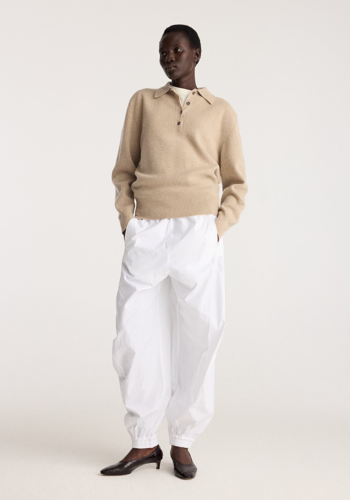 Wool cashmere polo | stone melange worn by a model with white trousers and black flats in a neutral studio setting