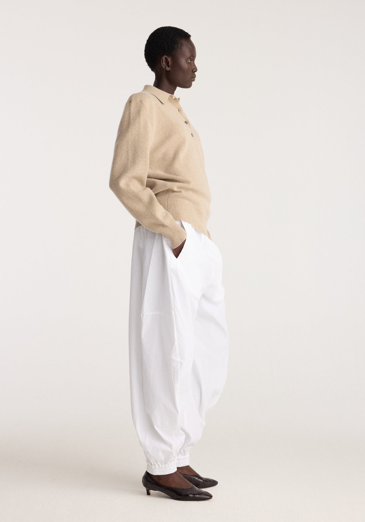 Model in Wool cashmere polo | stone melange with white trousers and dark leather shoes against a neutral studio background