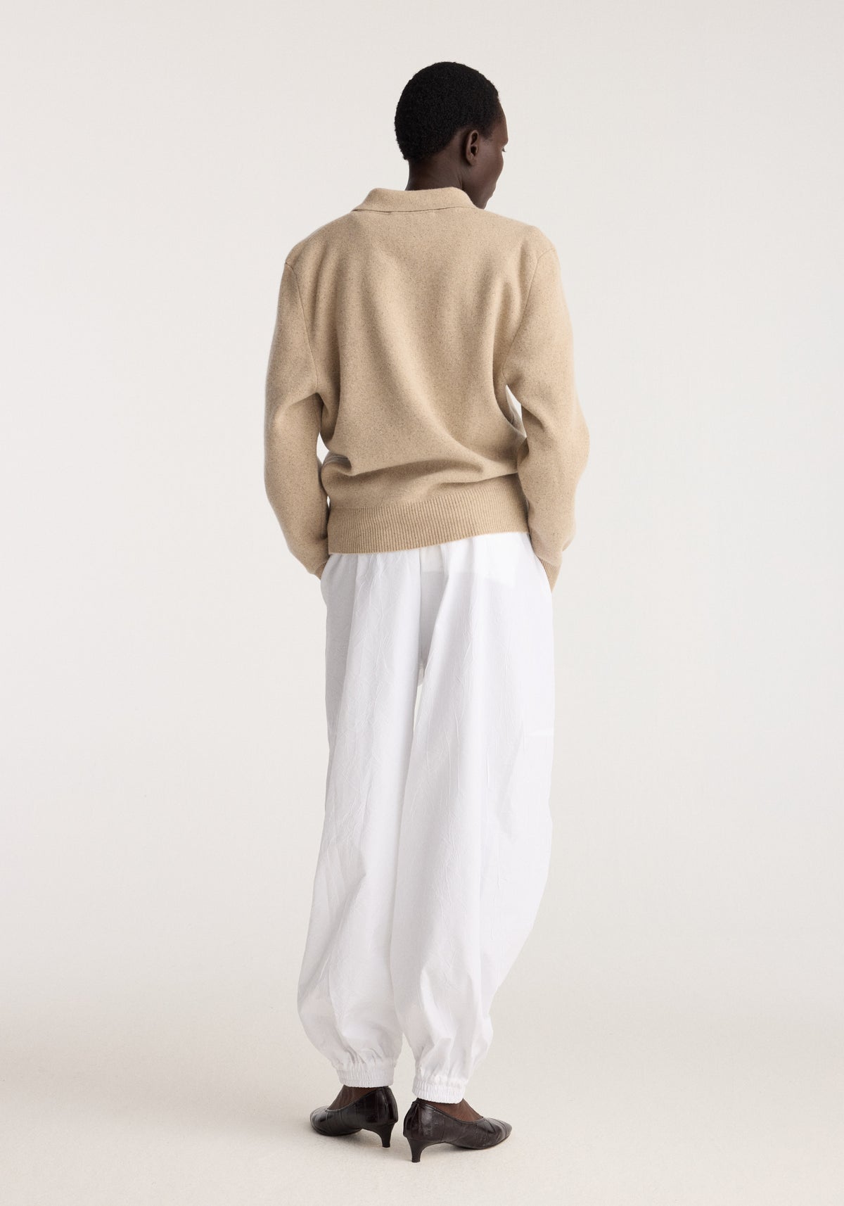 Wool cashmere polo | stone melange shown from the back on a model wearing white trousers and dark shoes