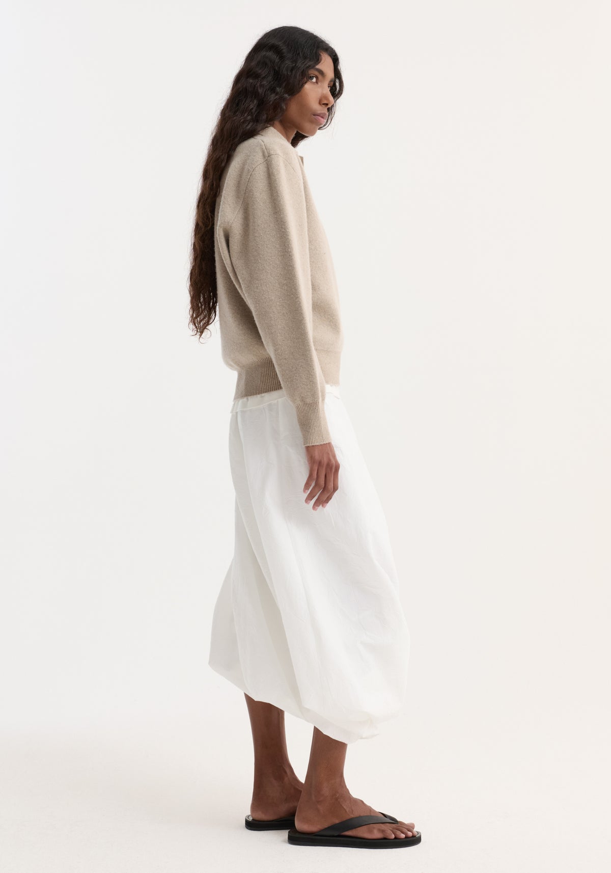 Side-profile of person in a light beige Wool cashmere polo with structured collar and three-button closure, paired with a flowing skirt.
