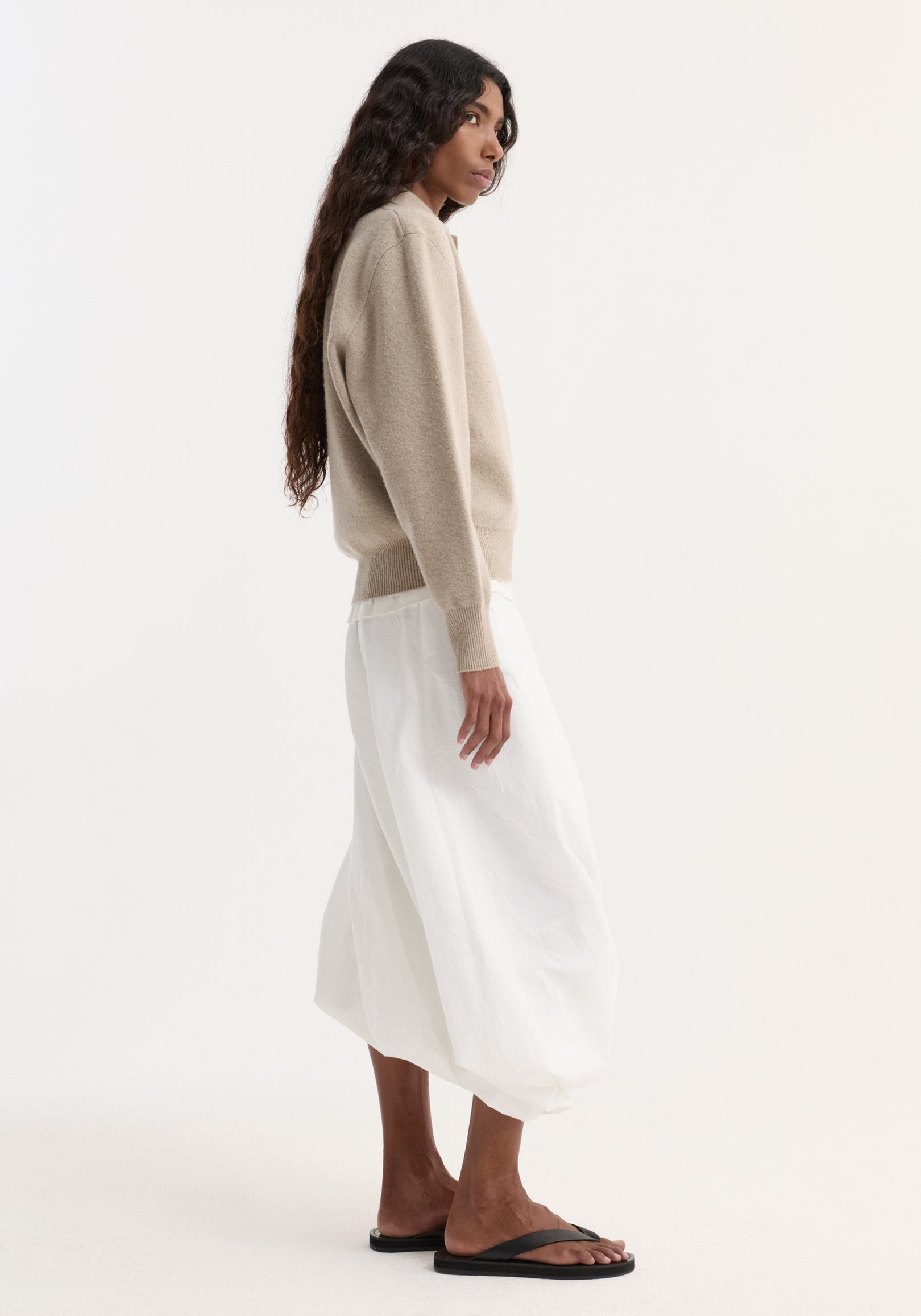 Side-profile of person in a light beige Wool cashmere polo with structured collar and three-button closure, paired with a flowing skirt.