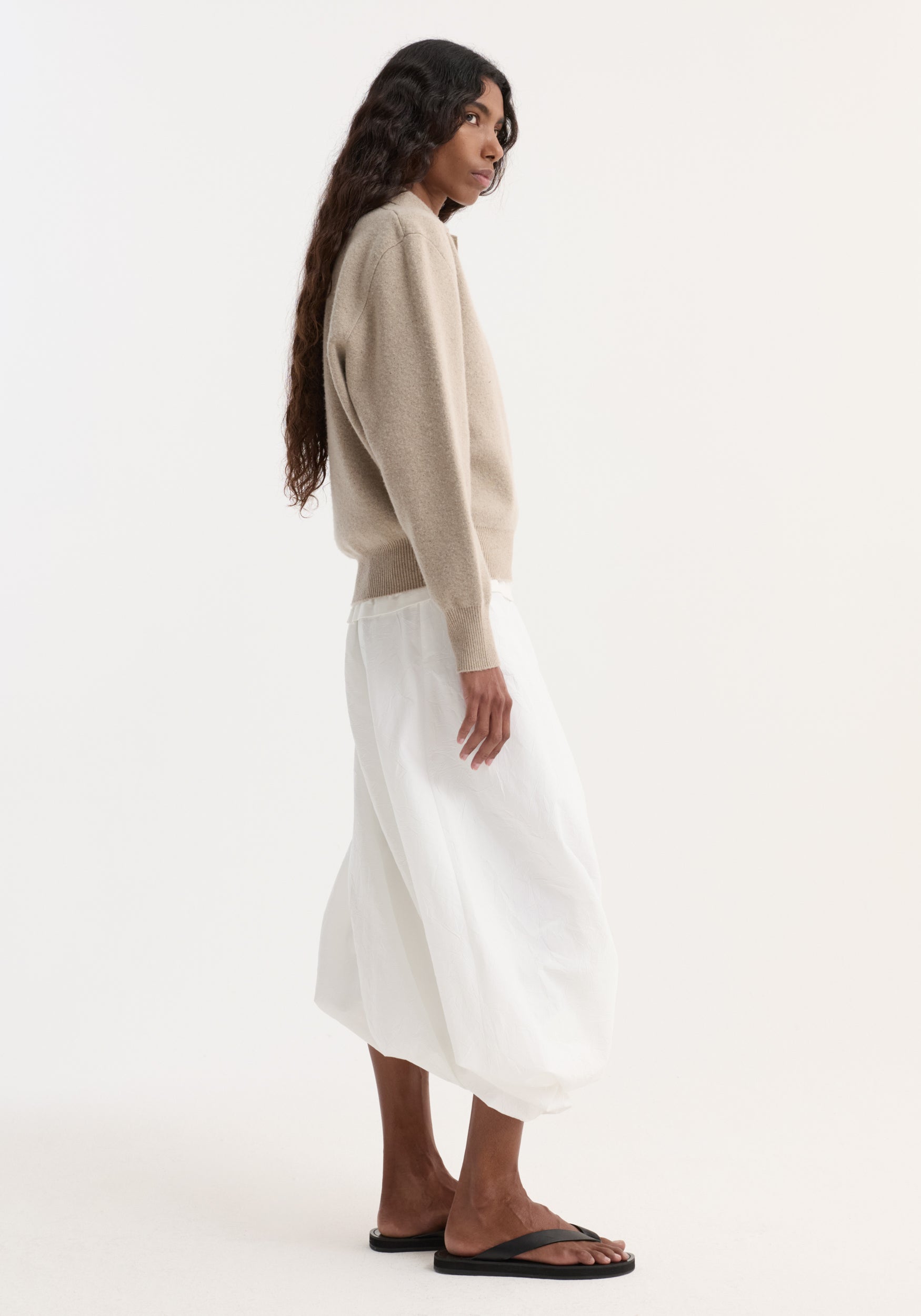Side-profile of person in a light beige Wool cashmere polo with structured collar and three-button closure, paired with a flowing skirt.