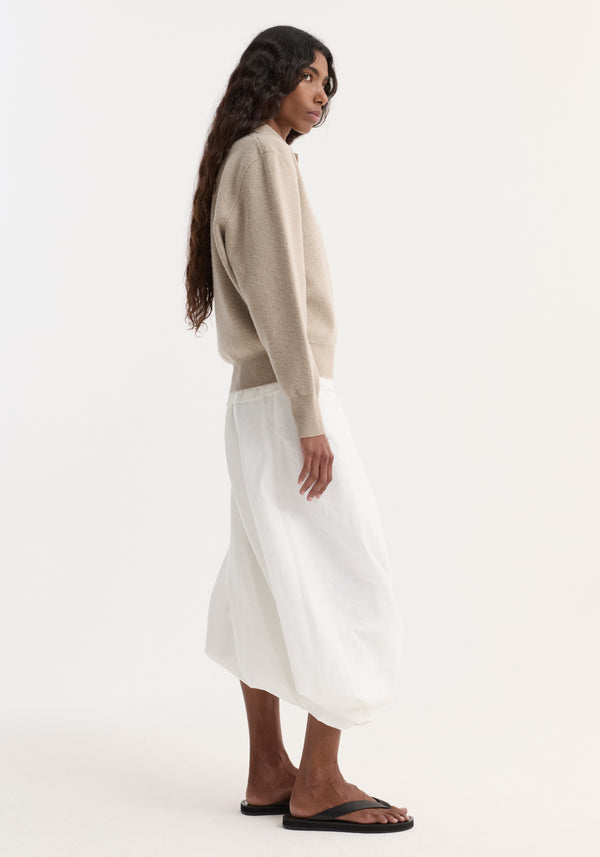 Side-profile of person in a light beige Wool cashmere polo with structured collar and three-button closure, paired with a flowing skirt.