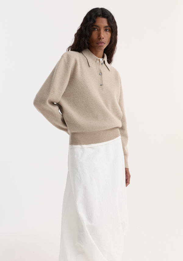 Model wearing a Wool Cashmere Polo in stone melange, featuring a structured collar and three-button closure, paired with a white midi skirt.