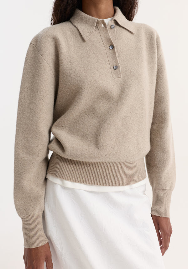 Wool cashmere polo in stone melange, featuring a structured collar, three-button placket, and ribbed cuffs, layered over a white top, tucked into a white skirt.