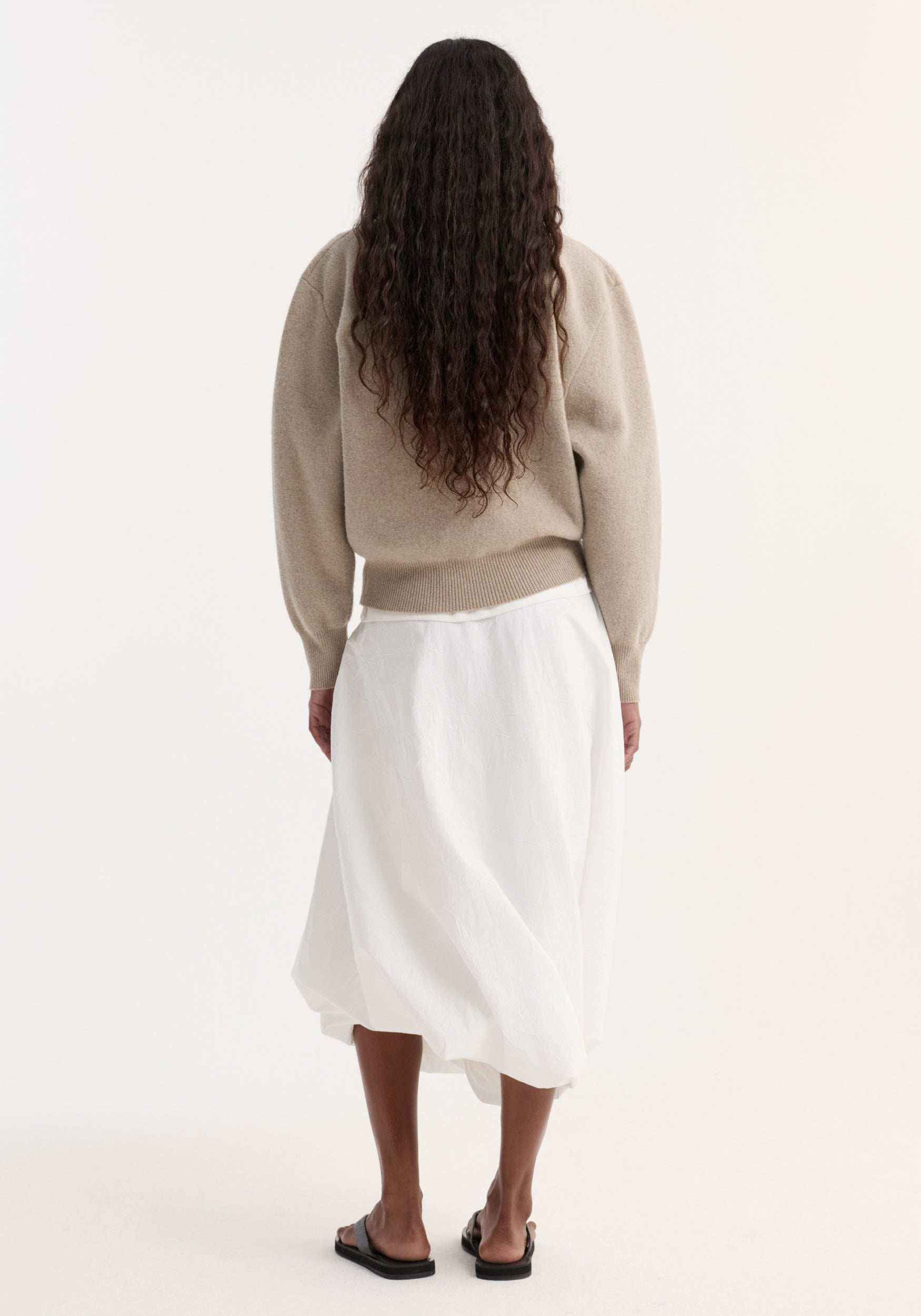 Back view of person wearing a Wool Cashmere Polo in stone melange, tucked into a white midi skirt, highlighting the knit's structured collar and button closure.