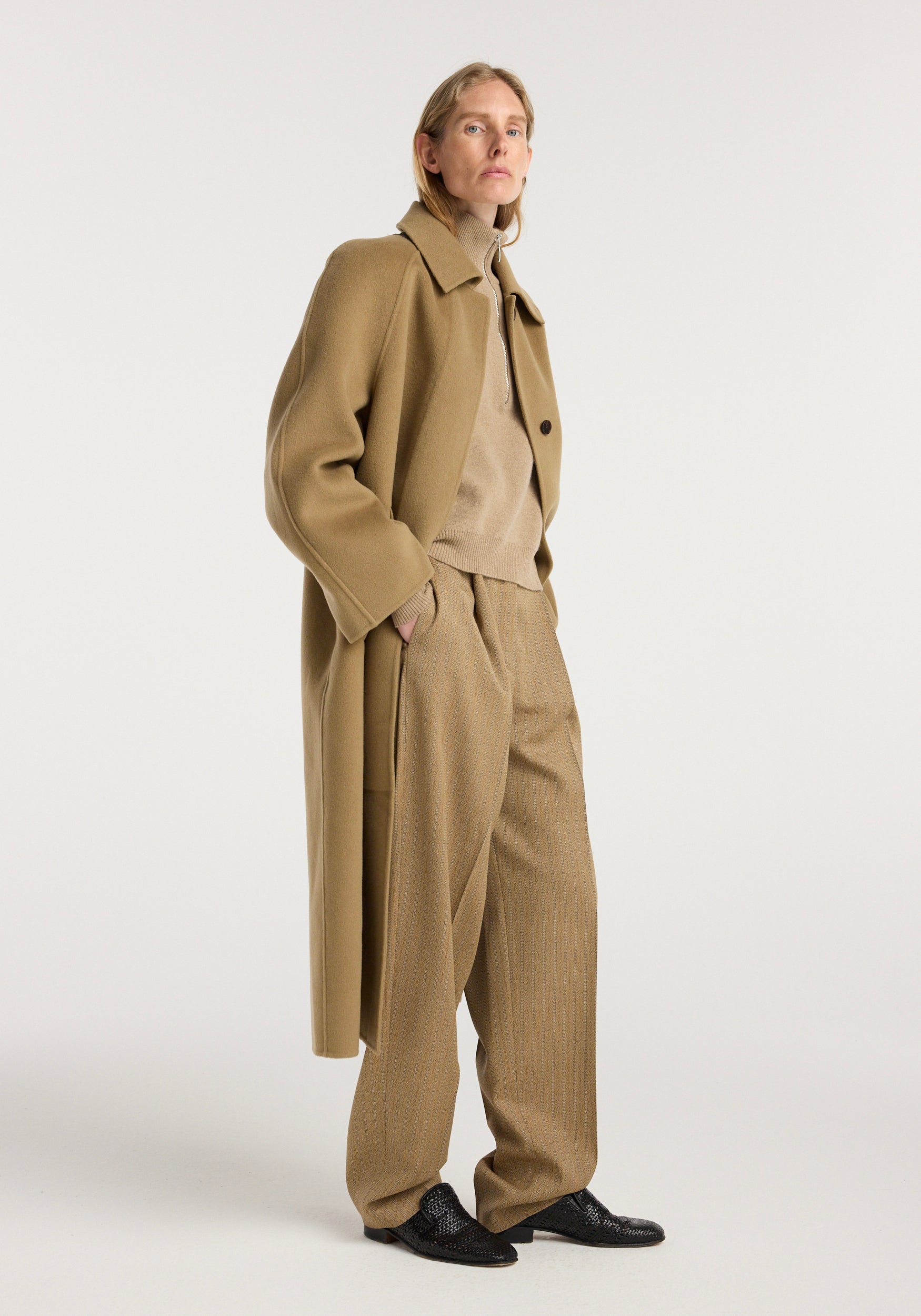 Woman wearing a camel-colored double-faced wool padded coat over a beige turtleneck and matching wide-leg trousers, styled with black textured shoes, standing against a plain background.