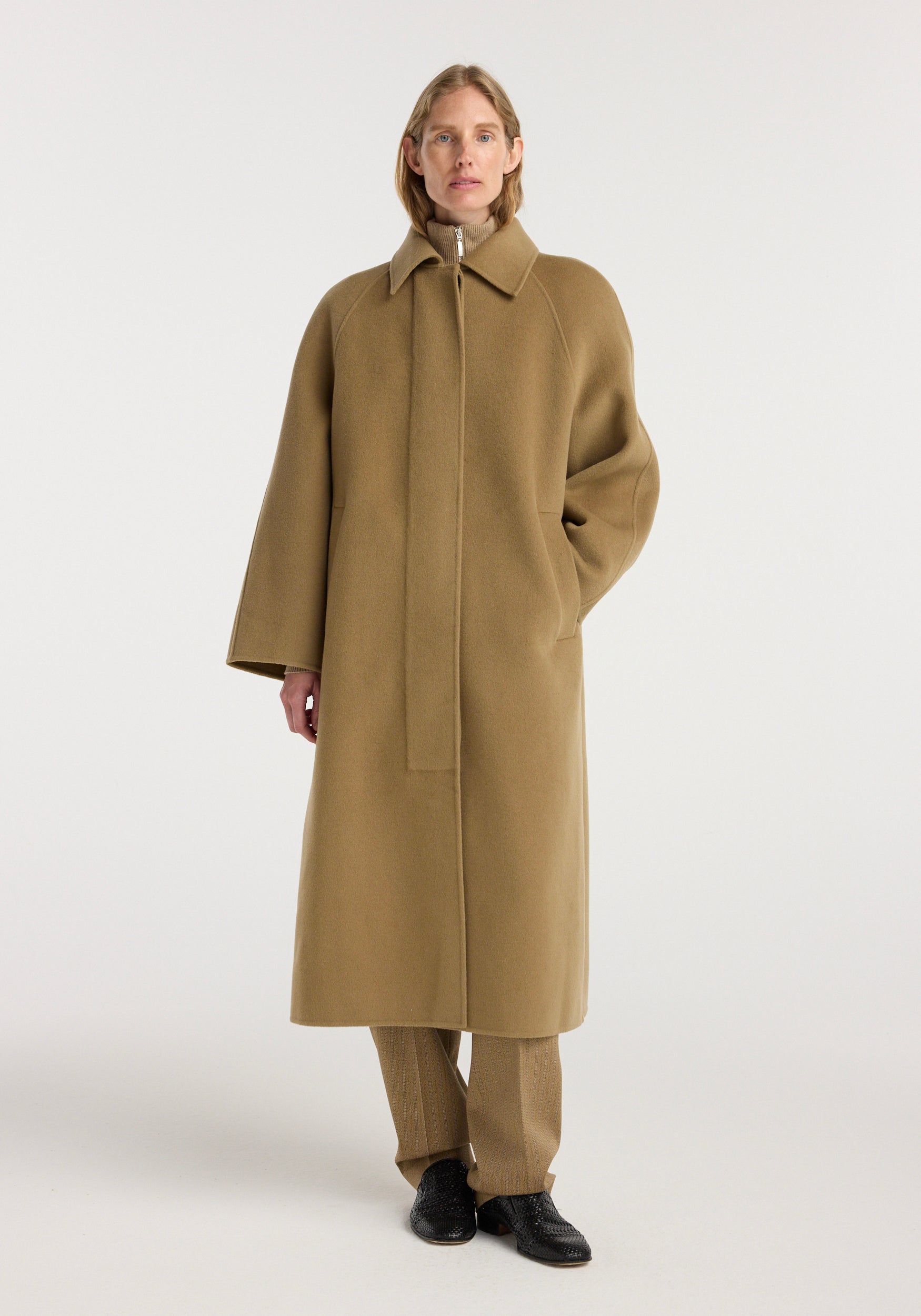 A model wearing a long camel-colored Double-faced wool padded coat | camel with a classic collar and concealed front closure, styled with matching pants and black shoes.